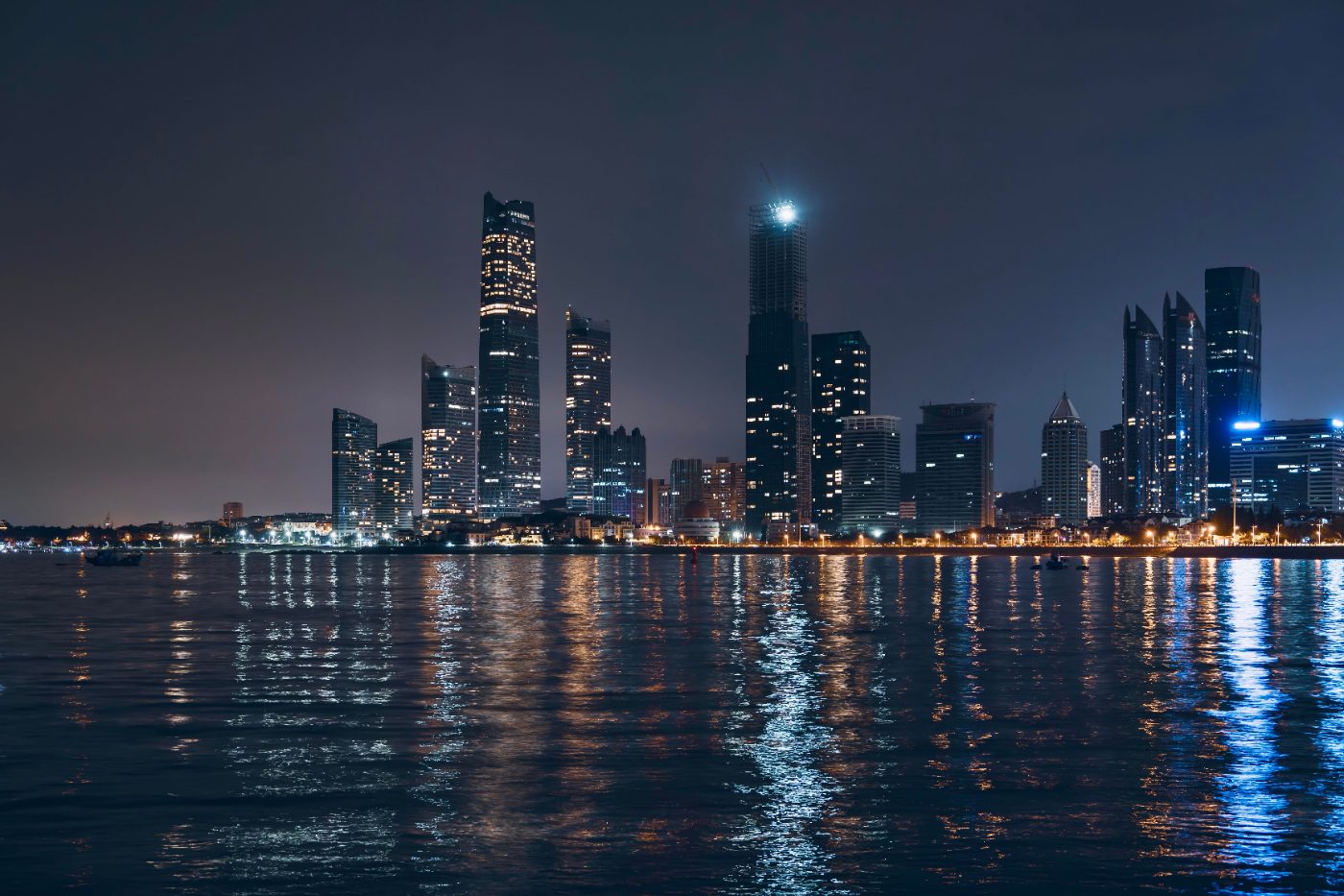 Night view of Abu Dhabi skyline with reflections on water, showcasing modern architecture.