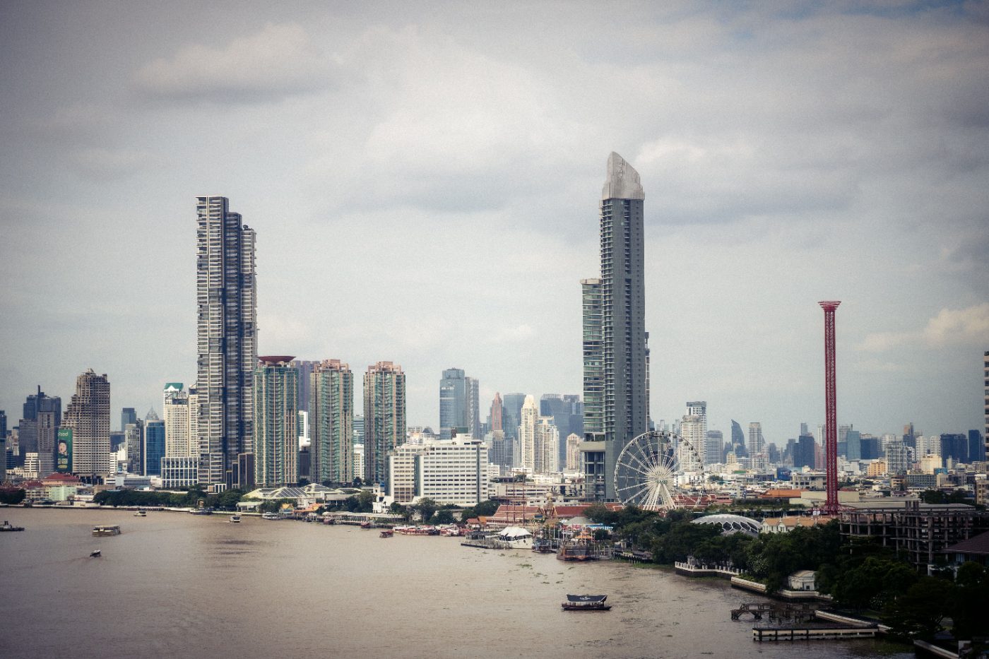 View of Bangkok skyline with iconic Ferris wheel and Chao Phraya River during the day.