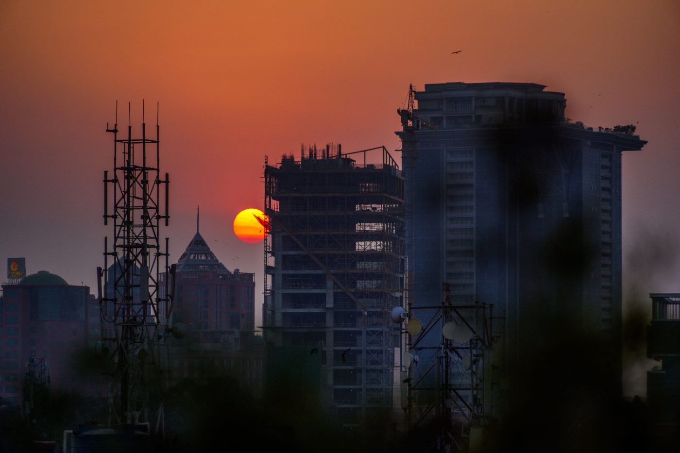 A dramatic skyline of Bengaluru with a vivid sunset highlighting tall buildings and communication towers.