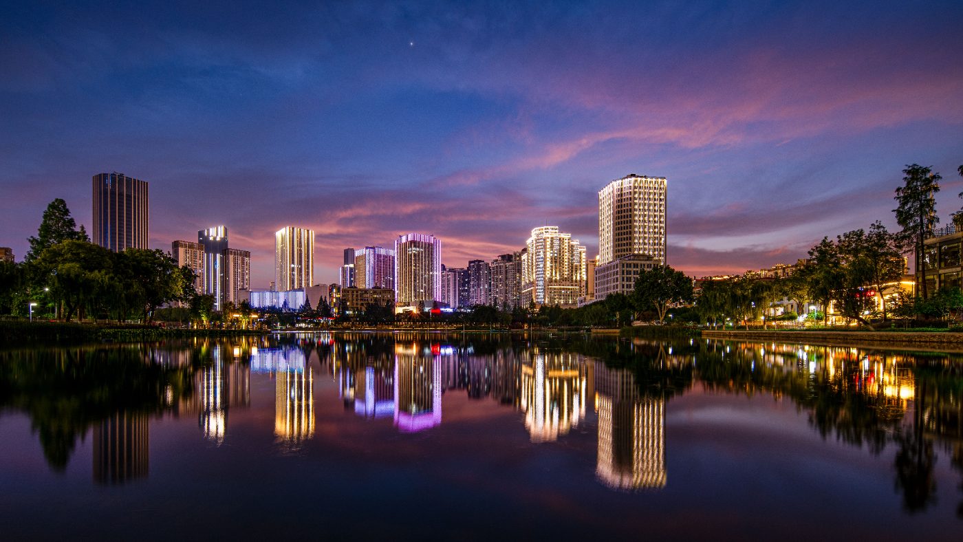 Vibrant city skyline with modern architecture reflected in a serene lake during twilight.
