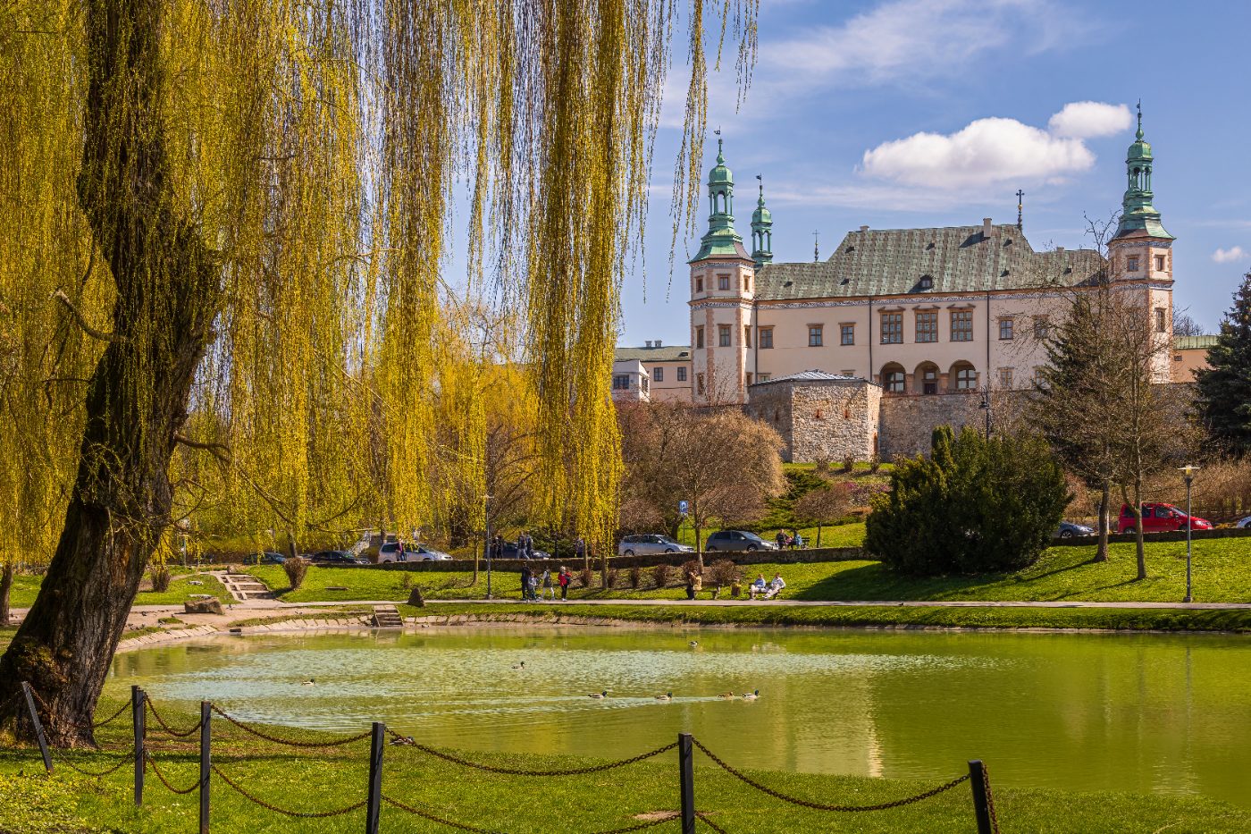 A beautiful park scene with a willow tree and historical building in Poland.