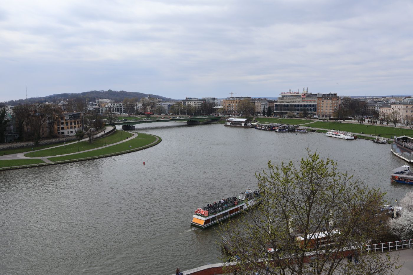 A picturesque aerial view showcasing boats on a river in an urban park setting under cloudy skies.