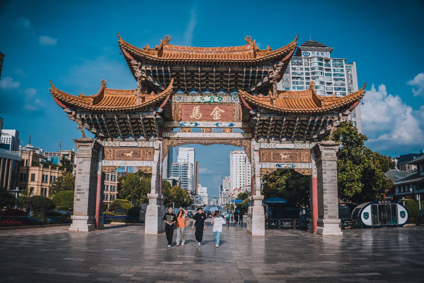 Traditional Chinese archway against Kunming city backdrop, attracting tourists.