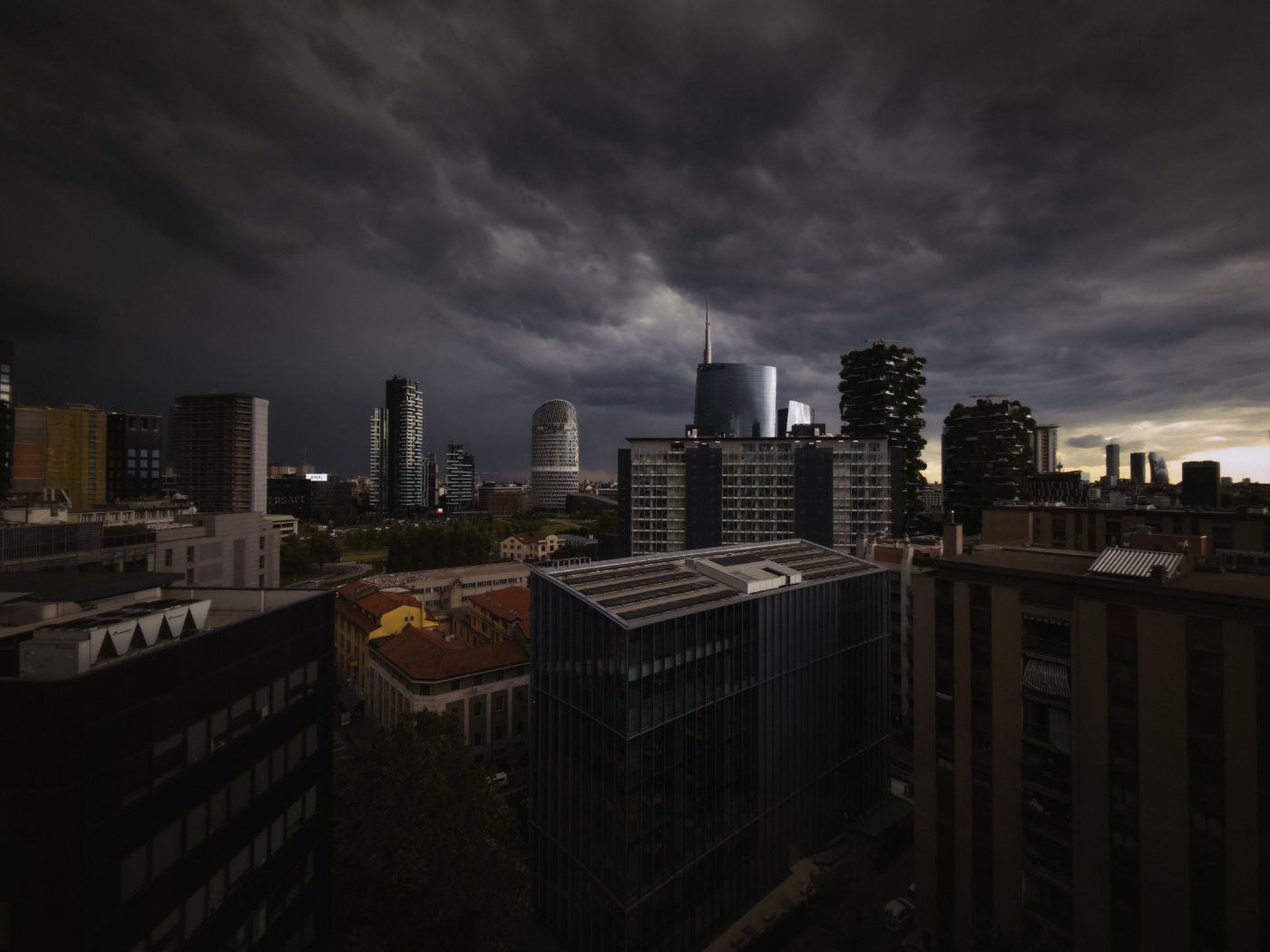 A dark, stormy sky looms over a modern urban skyline at dusk, creating a dramatic cityscape.