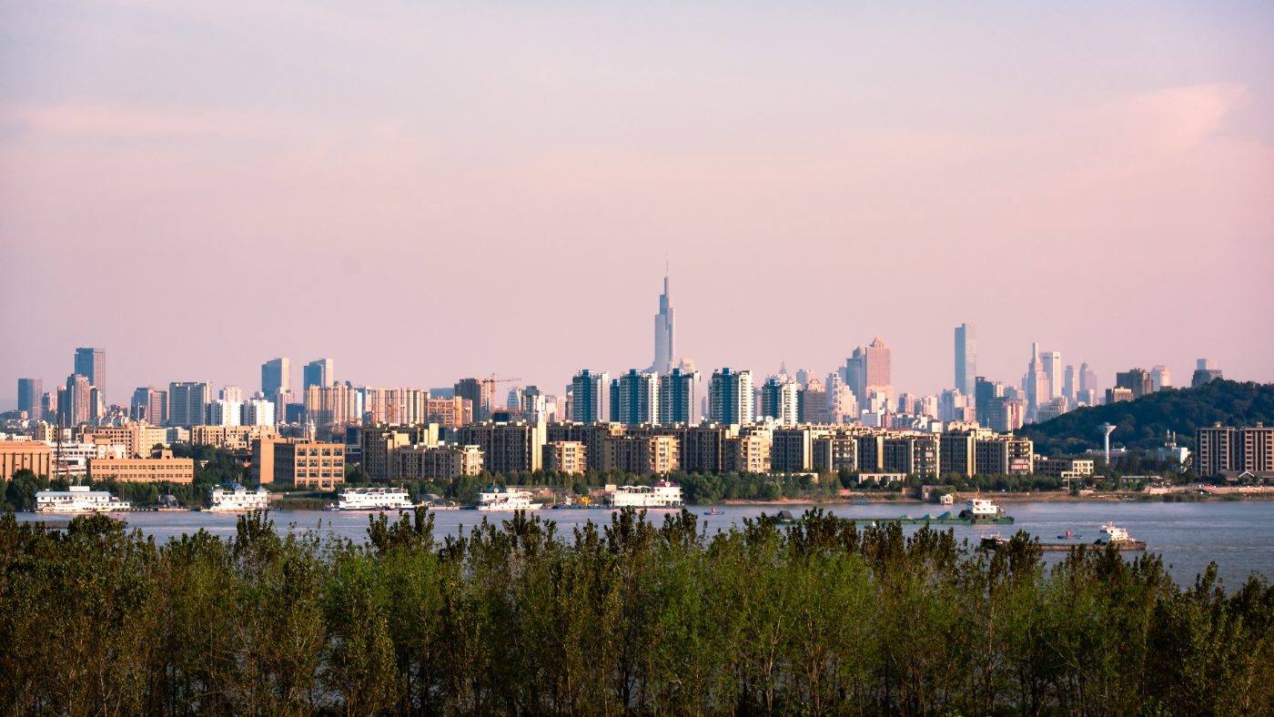Panoramic view of a vibrant city skyline across a tranquil river during daytime.