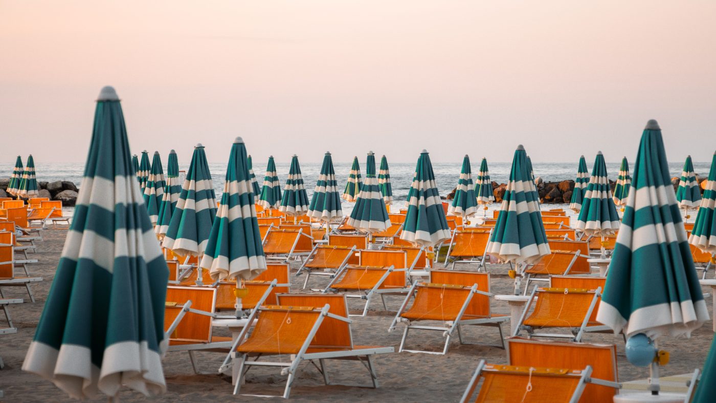 Colorful striped umbrellas and chairs on Rimini beach during sunset, perfect for summer vibes.