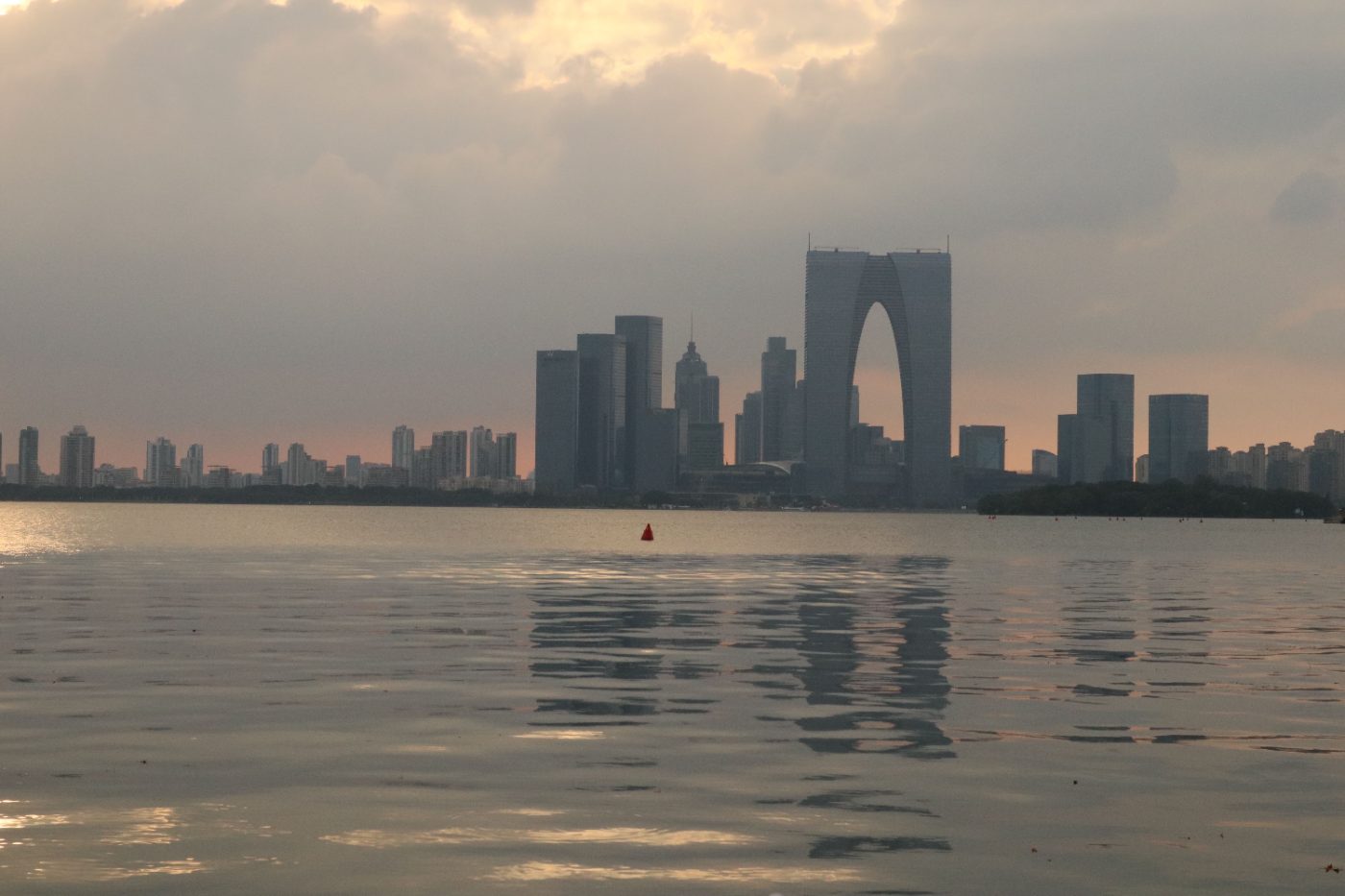 Serene sunset view of Suzhou skyline reflected over Jinji Lake with moody clouds.