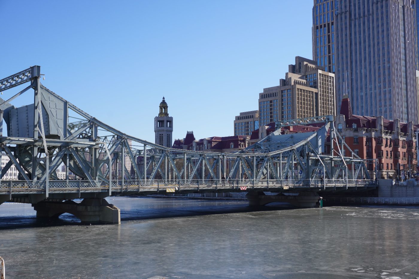 Jiefang Bridge in Tianjin showcasing urban architecture and the frozen Haihe River under a clear blue sky.