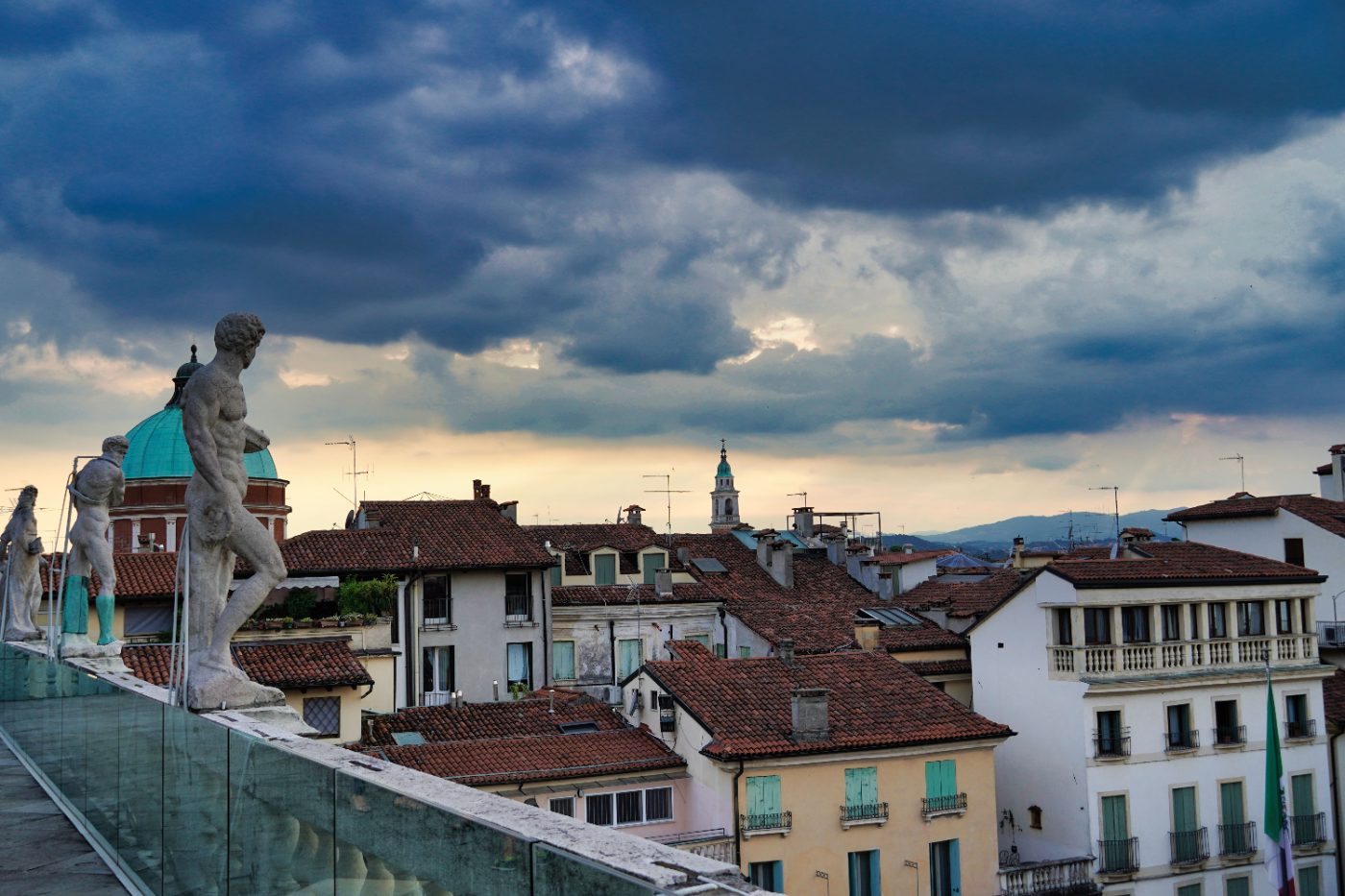 View of Vicenza rooftops and statues under a dramatic evening sky.