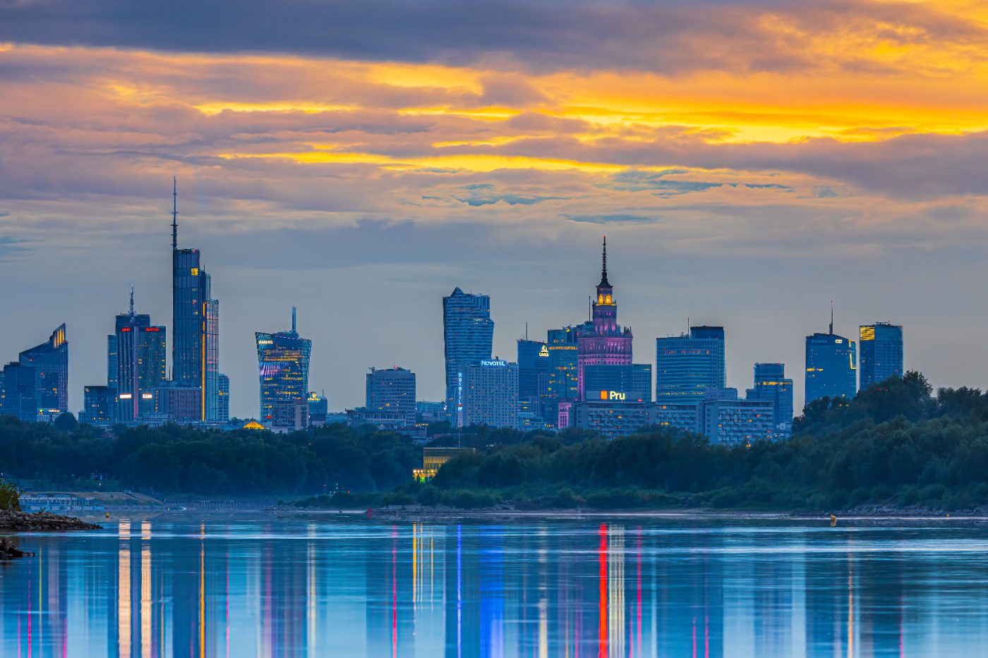 Experience the vibrant Warsaw skyline at sunset, reflecting beautifully in the river.