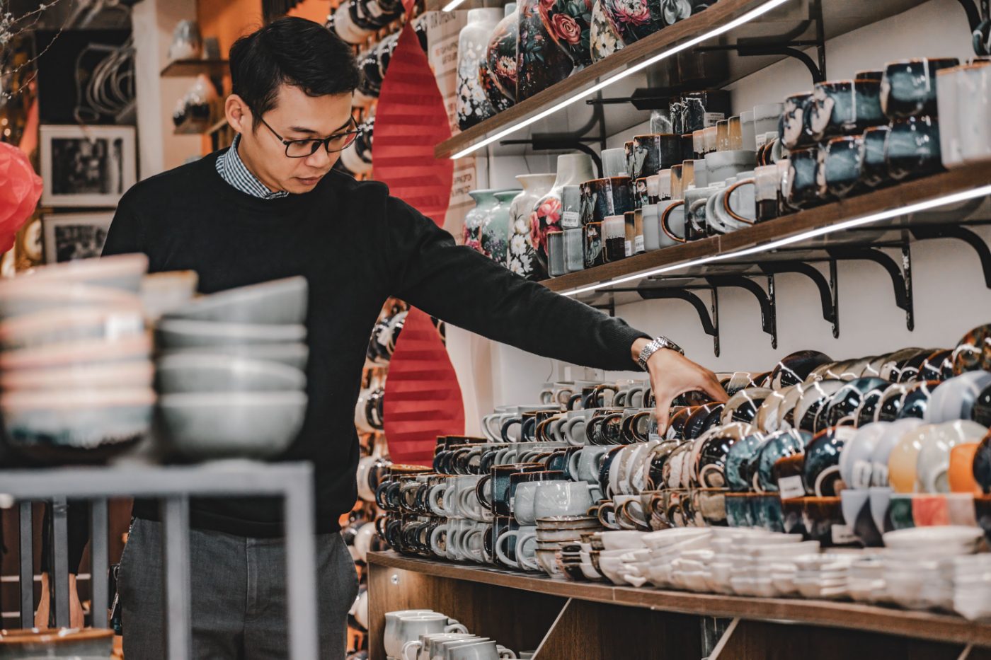 A man browsing a variety of ceramic mugs and bowls inside a shop in Hanoi, Vietnam.