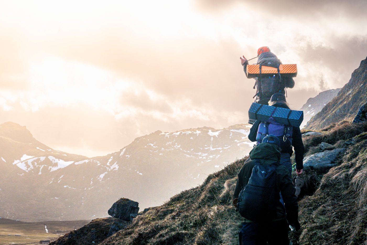 A group of hikers trekking up a mountainous trail in Nordland, Norway at sunset.